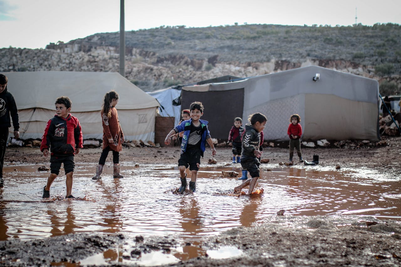 who-we-are Kids enjoying playtime in a muddy refugee camp in Idlib, Syria amidst challenging conditions.