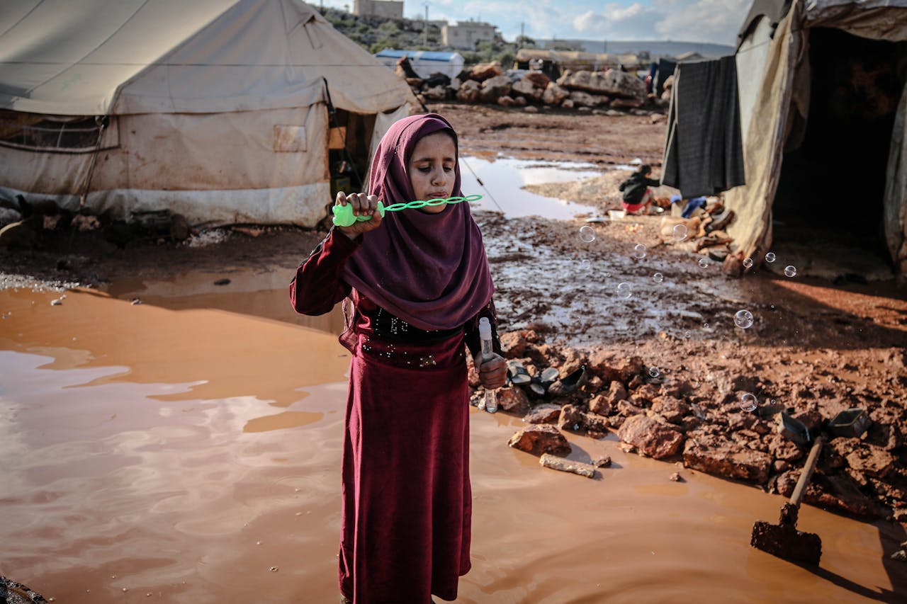 services-04 A young girl in Idlib refugee camp blowing bubbles, symbolizing innocence amidst adversity.