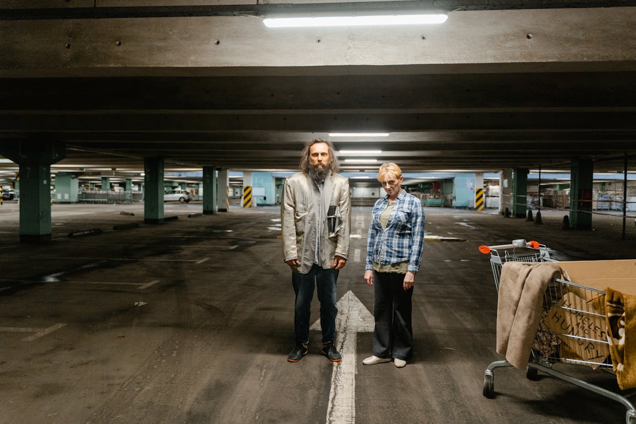 Elderly man and woman stand in a parking garage, symbolizing urban homelessness.