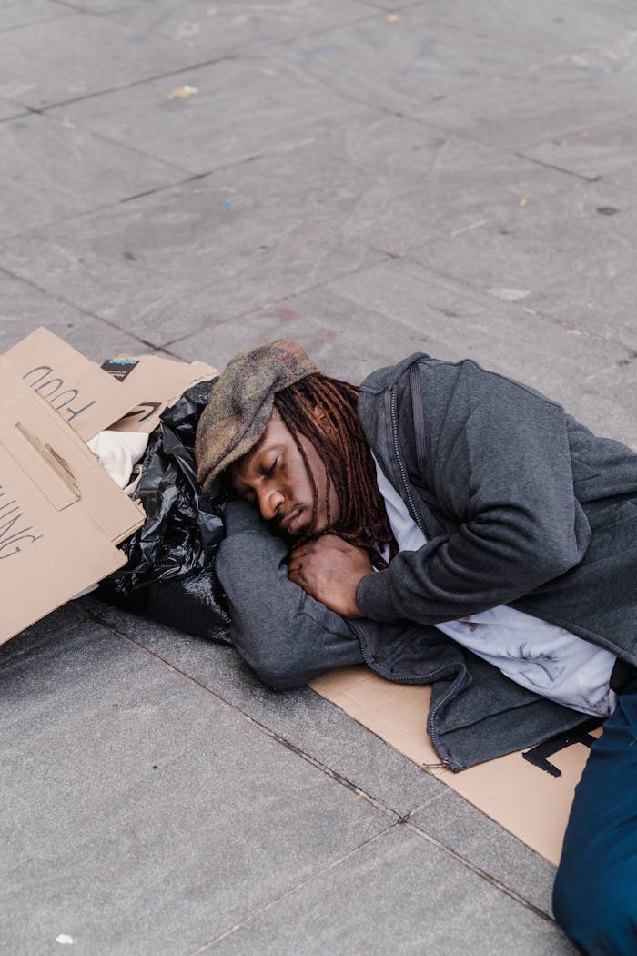 services-01 A homeless man sleeping on the street with cardboard signs and belongings.